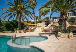 a swimming pool with palm trees and a house at Villa Linda in Punta Prima