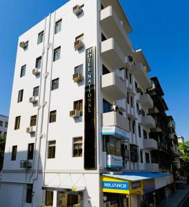 a white building with a man sitting on a balcony at Hotel National - Grant Road in Mumbai
