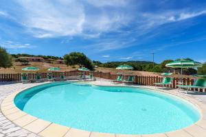 a large swimming pool with chairs and umbrellas at Casa Mirto con piscina e vista mare in Aglientu