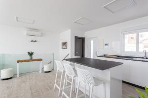 a white kitchen with a black counter and white stools at Nerja Luxury Apartment in Nerja +14 photos