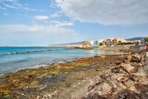 a beach with rocks and the ocean and buildings at Sunrise Arinaga in Arinaga