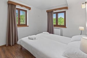 a white bedroom with two beds and two windows at Holiday Home Pahari by Rent Istria in Roč