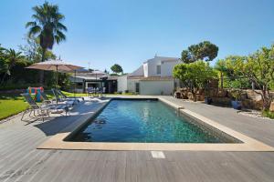 a swimming pool with chairs and an umbrella next to a house at Pine Lodge in Vilamoura
