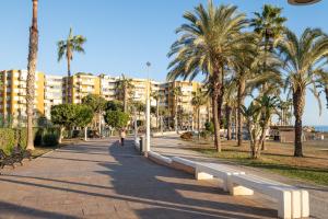 a person walking down a sidewalk with palm trees and condos at Casa Santo front beach in Cala del Moral