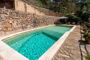 a swimming pool with a stone wall and blue water at Es Racó d'Alconàsser in Sóller