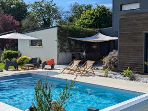 a pool with chairs and umbrellas in a backyard at La Fée Maison, chambres d'hôtes in Plouër-sur-Rance