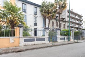 a white building with palm trees in front of a street at Le Béout rez-de-jardin in Lourdes