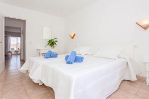 a white bedroom with a large white bed with blue pillows at Cala'n Blanes Park 228 in Cala en Blanes