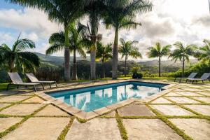 a swimming pool with two chairs and palm trees at Villa Kamaya, Chamarel in Chamarel