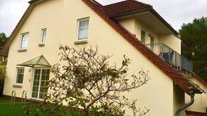 a white house with a balcony and a tree at Sommergarten mit Winternutzung in Karlshagen