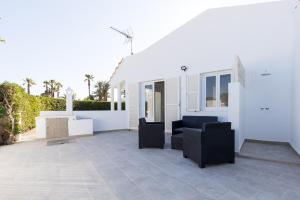a patio with black chairs and a white house at Chalet a 150m de la playa y piscina privada in Cala en Bosc