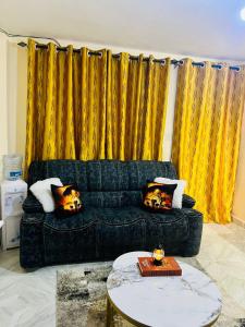 a black couch in a living room with yellow curtains at Nimaai Apartment in Narok