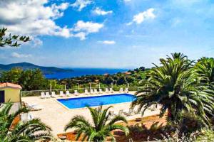 a swimming pool with palm trees and a view of the ocean at Mono Le Lecce 25 b in Capoliveri
