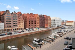 a city with cars parked next to a river with buildings at Waterlane Riverside - SPA, Pool, Gym & Parking by Downtown Apartments in Gdańsk +70 photos