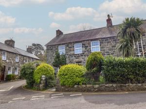 an old stone house with bushes in front of a street at Glanrafon in Llwyngwril