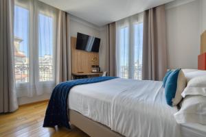 a bedroom with a bed and a tv and windows at Hôtel de Bellevue Paris Gare du Nord in Paris