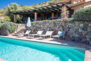 a swimming pool with chairs and a stone wall at Fantastica Villa con piscina e vista mare in Alghero