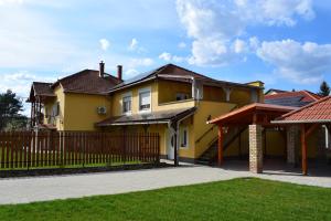 a yellow house with a fence and grass at Sódomb vendégház in Egerszalók