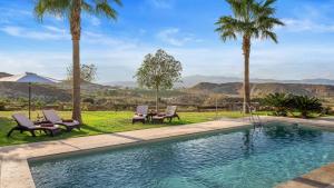 a swimming pool with two chairs and palm trees at Boutique Hideaway Cortijo El Sarmiento - Adults Only in Mojácar