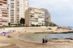 a group of people standing on a beach with buildings at Cala Morelló in Ifach