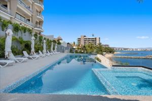 a swimming pool next to a building with chairs at Bahiban Residences Oceanfront by Monyxbnb in Cruz de Huanacaxtle