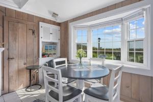 a dining room with a table and chairs and windows at The Shell Cottage - Where Beach Dreams Begin in South Yarmouth