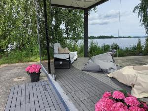 acovered deck with flowers and a chair and a view of the water at Piestātne Riverside Cabins with Sauna, Hot Tub & Private Pier in Katlakalns