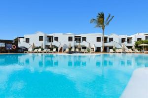 a large swimming pool with chairs and a palm tree at R2 Bahia Kontiki in Puerto del Carmen