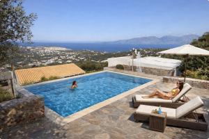two people are sitting in a swimming pool at Althea Villas by breathtaking view in Agios Nikolaos