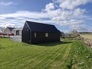 a black building in a field with a grass yard at Pleasant Point Holiday Cottages in Glenurguhart
