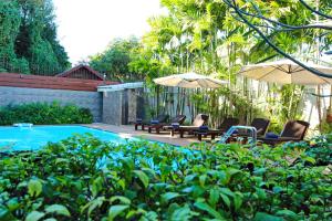a pool with chairs and umbrellas in a garden at Shewe Wana Boutique Hotel in Chiang Mai