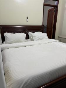 a large white bed with white sheets and pillows at Sahel Gardens in Kisubi