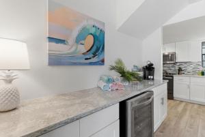 a kitchen with white cabinets and a painting on the wall at Be A Nomad - 2BR Jacksonville Beach Apartment - 1 Min to Beach - Sleeps 4 in Jacksonville Beach