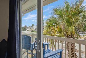 a balcony with two blue chairs and a palm tree at Be A Nomad - 2BR Jacksonville Beach Apartment - 1 Min to Beach - Sleeps 4 in Jacksonville Beach