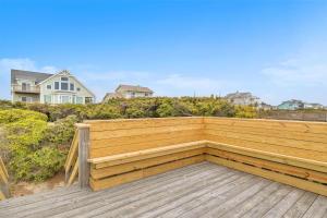 a wooden bench on a deck with a house in the background at Azohva by Oak Island Accommodations in Caswell Beach