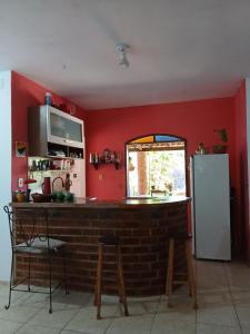 a kitchen with a red wall with a counter and a refrigerator at Quarto Privativo e Camping em Canoa Quebrada in Canoa Quebrada