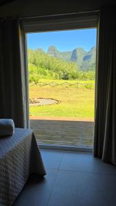 a bedroom with a large window with a view of a field at CASA GRÊS - Pousada Vale das Escarpas in Timbe do Sul