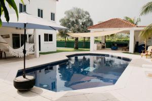 a swimming pool with an umbrella and a house at Casa La Yola in Monterrico