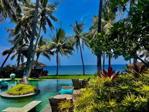 a resort pool with palm trees and the ocean at Louka Beach Bali in Tianyar