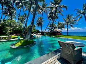 a swimming pool with palm trees and the ocean at Louka Beach Bali in Tianyar