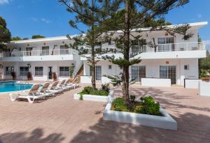 a large white building with lounge chairs and a swimming pool at Hostal Es Pi - Emar Hotels in Playa Migjorn