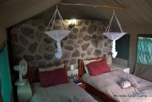 1 dormitorio con 2 camas y pared de piedra en Mondjila Safari Camp, en Okaukuejo