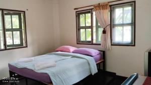 a bedroom with a bed with purple pillows and two windows at Ban Chomdoi บ้านชมดอย in Ban Dong