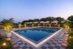 a pool at a resort with palm trees and umbrellas at Desert Horizon Luxury Resort &Camp in Jaisalmer