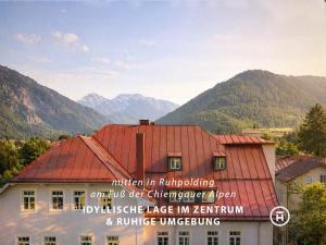 a building with a red roof with mountains in the background at The Townhouse Ruhpolding - Individual Design & Casual Concept - Chiemgau Karte in Ruhpolding
