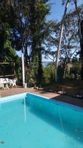 a blue swimming pool with a bench and trees at Pousada Recanto Dos Pássaros in Colégio