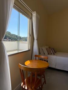 a bedroom with a table and a bed and a window at Suíte confortável no centro da cidade in Miguel Pereira