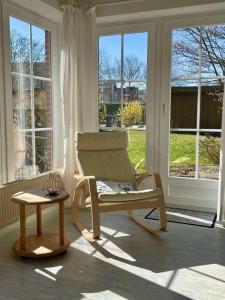 a rocking chair and a table in a room with windows at FeWo-mit-Terasse-u-Garten-am-Golfplatz in Wulfen auf Fehmarn +12 photos