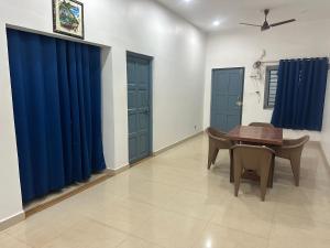 a dining room with blue curtains and a wooden table at Joy Villa Homestay in Honāvar