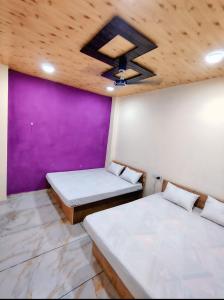 two beds in a room with a purple wall at Jay shree Kedar room in Ujjain